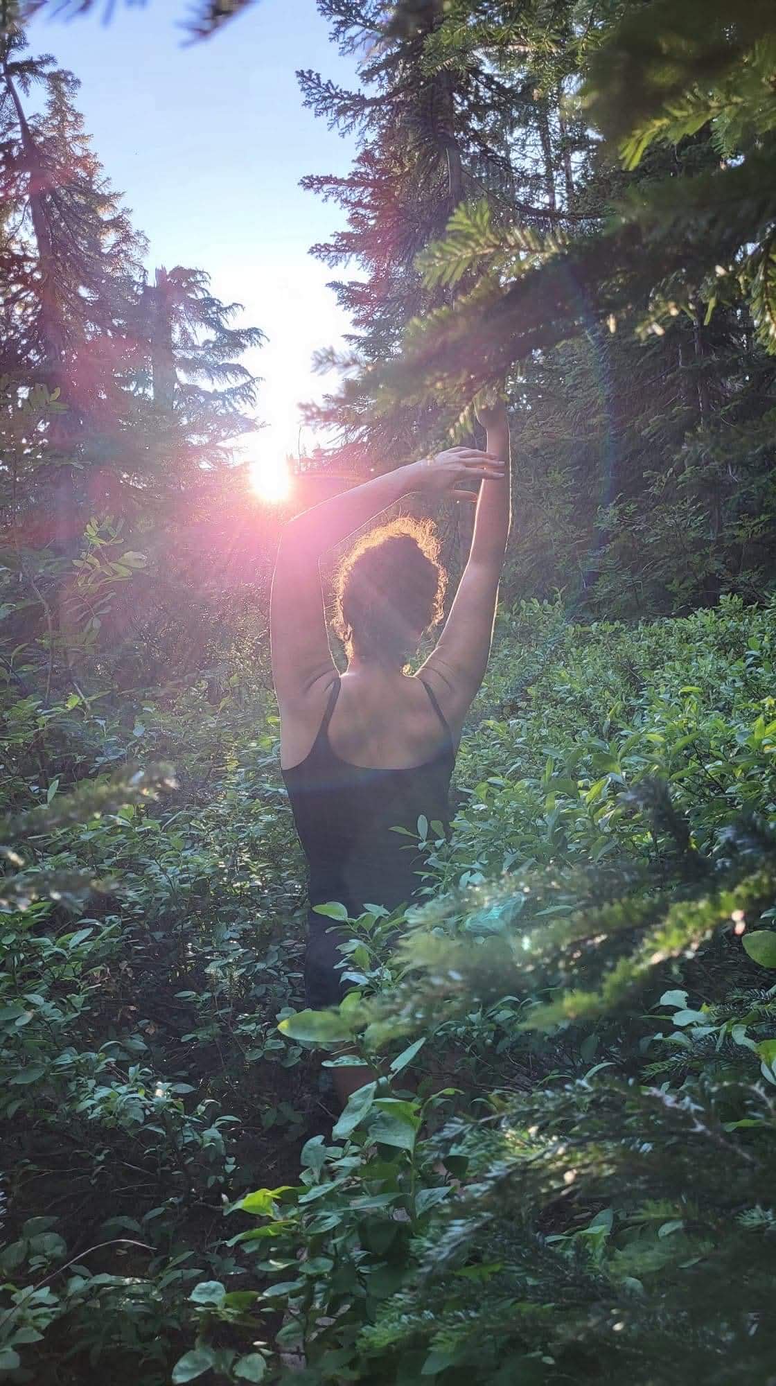Kirsten stretching toward the sunlight in a forest